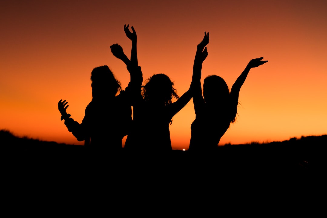 silhouette of three woman with hands on the air while dancing duri